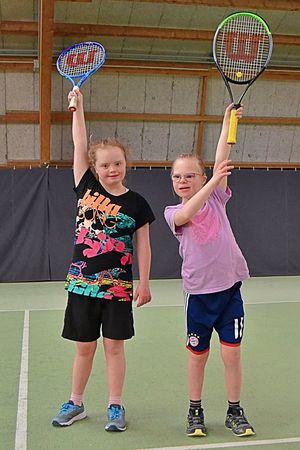 Zwei motivierte PluSportlerinnen halten ihre Tennisschläger in die Luft.